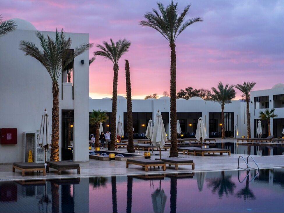 Resort pool and palm trees under a pink and purple sunset