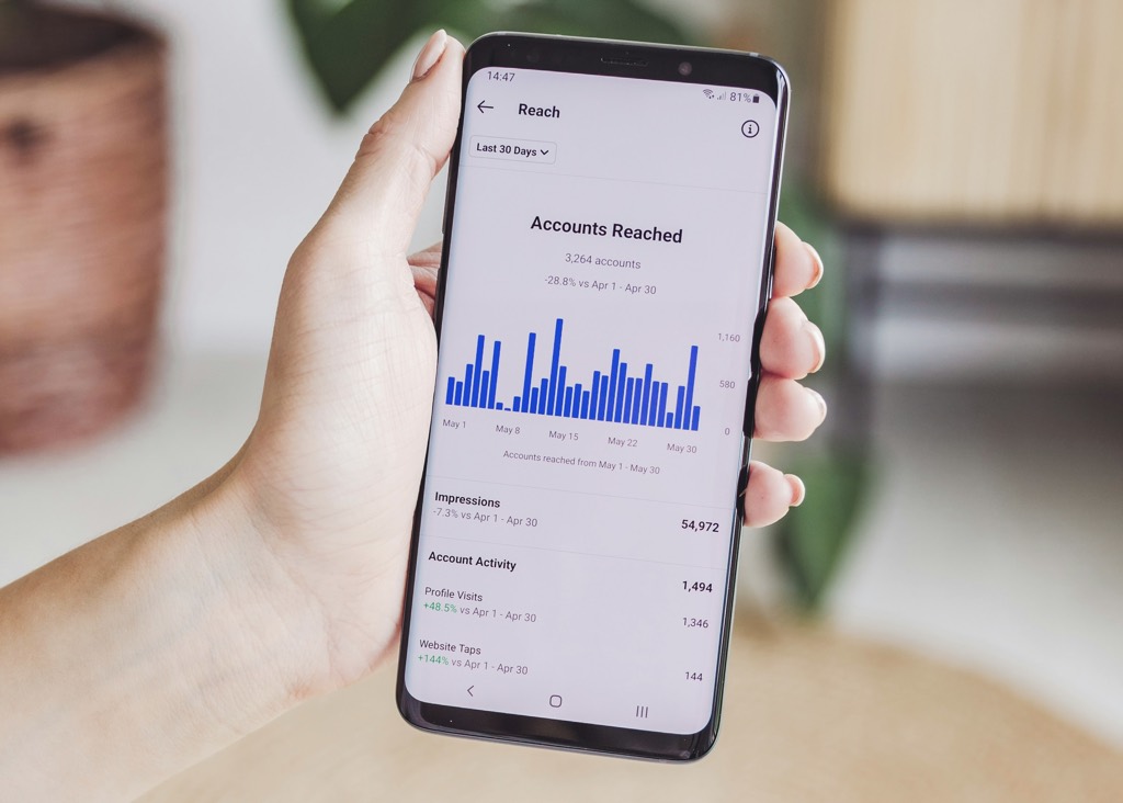 A hand holding a phone showing Instagram reach analytics
