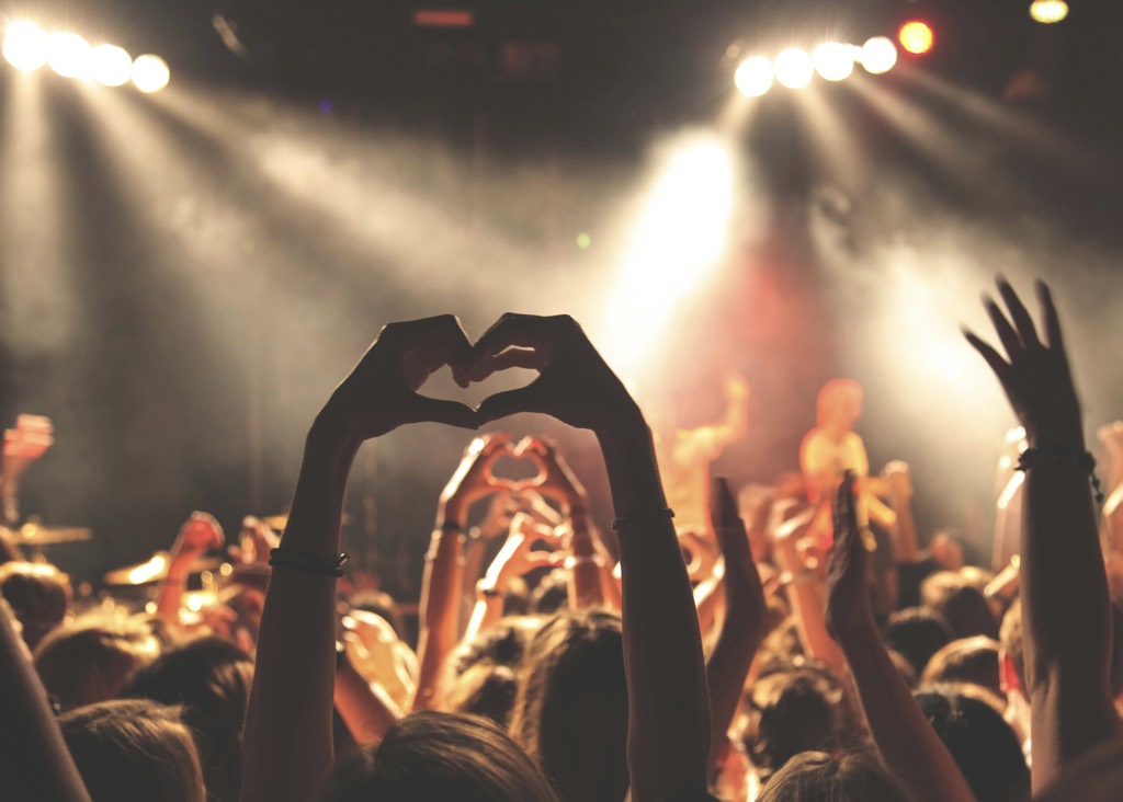 Concert crowd making a heart shape with their hands under stage lights